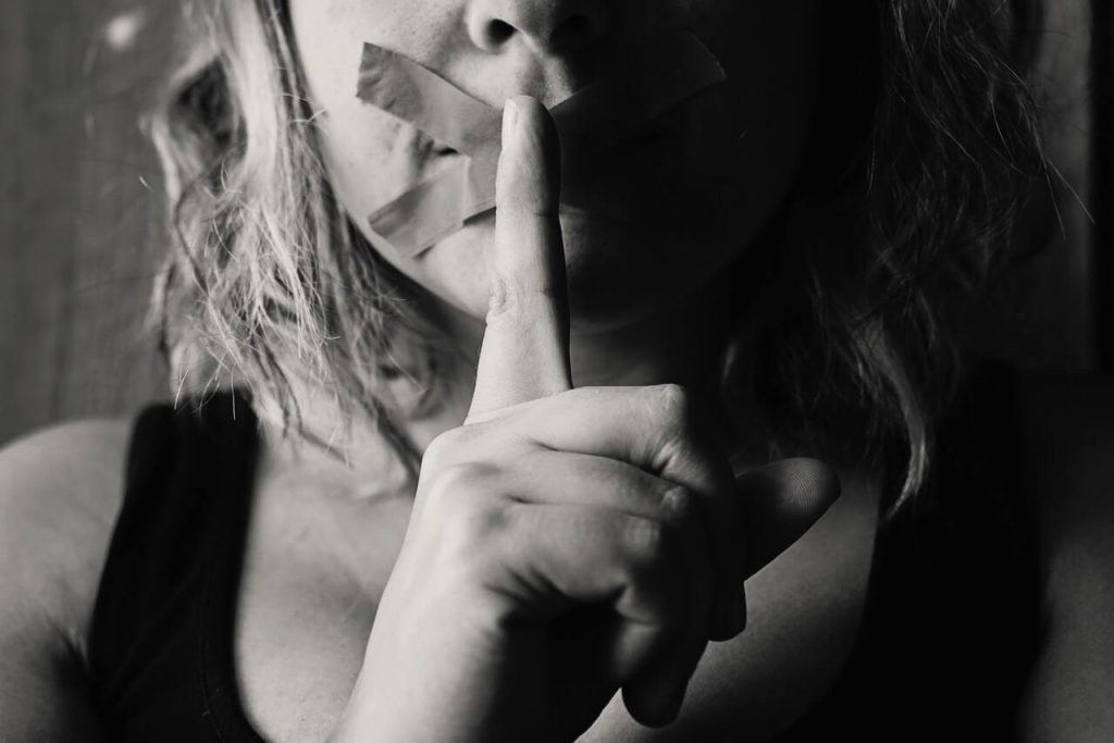 photo of a contemporary art of a woman with tape on her mouth and a finger to her mouth