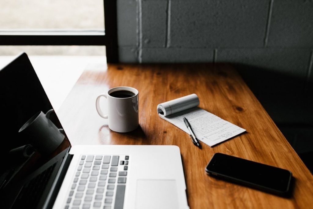 photo of a desk with a laptop, coffee, and notepad