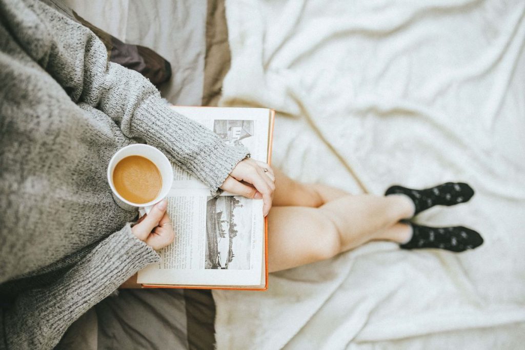 photo of a girl with a book her lap while holding a cup of coffee