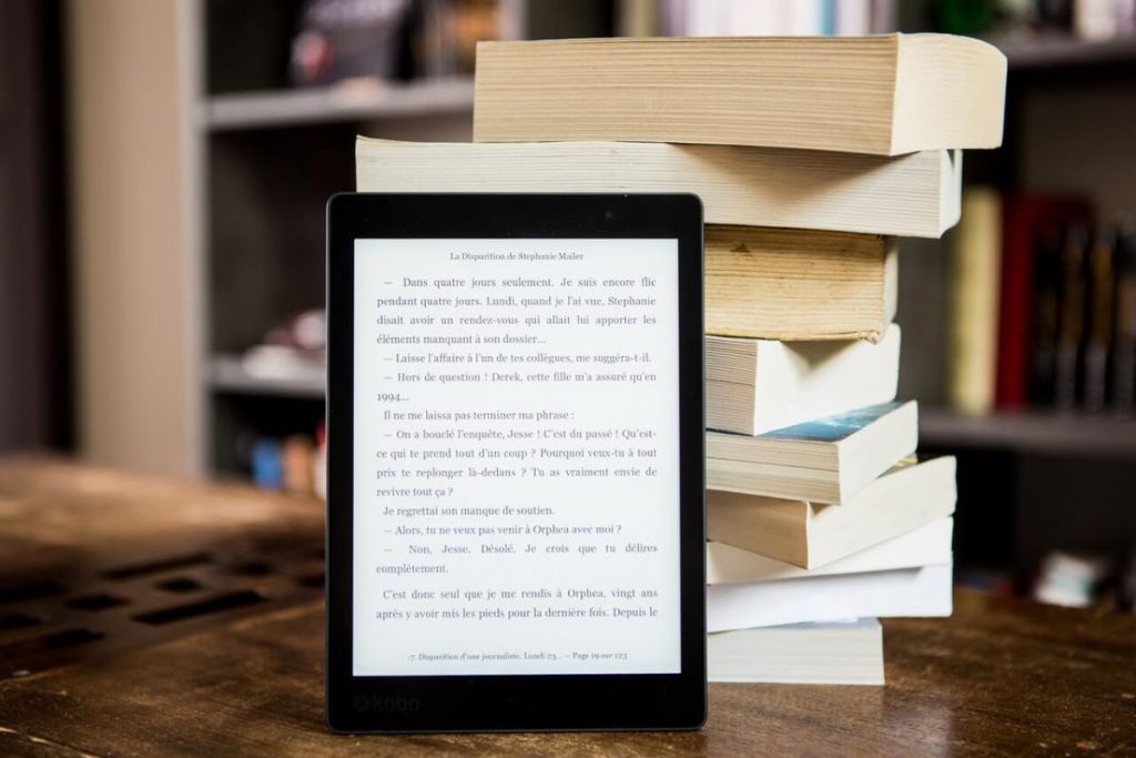 photo of a kindle leaning on a stack of books