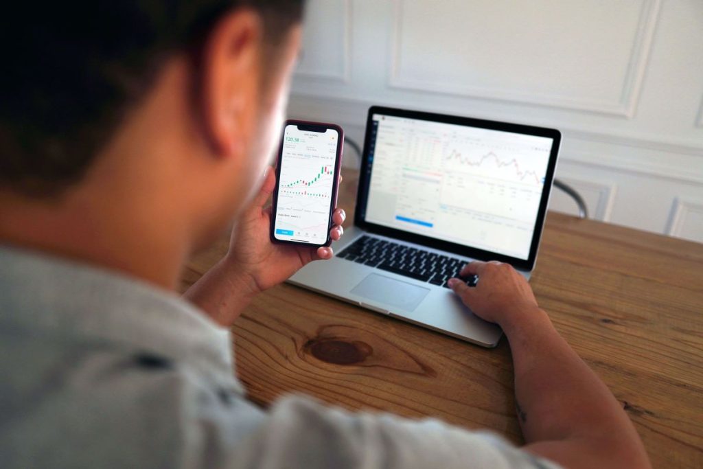 photo of a man checking the stock market on his phone and laptop