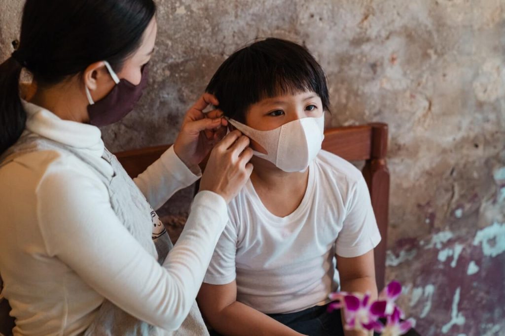 photo of a mother putting a facemask on her son