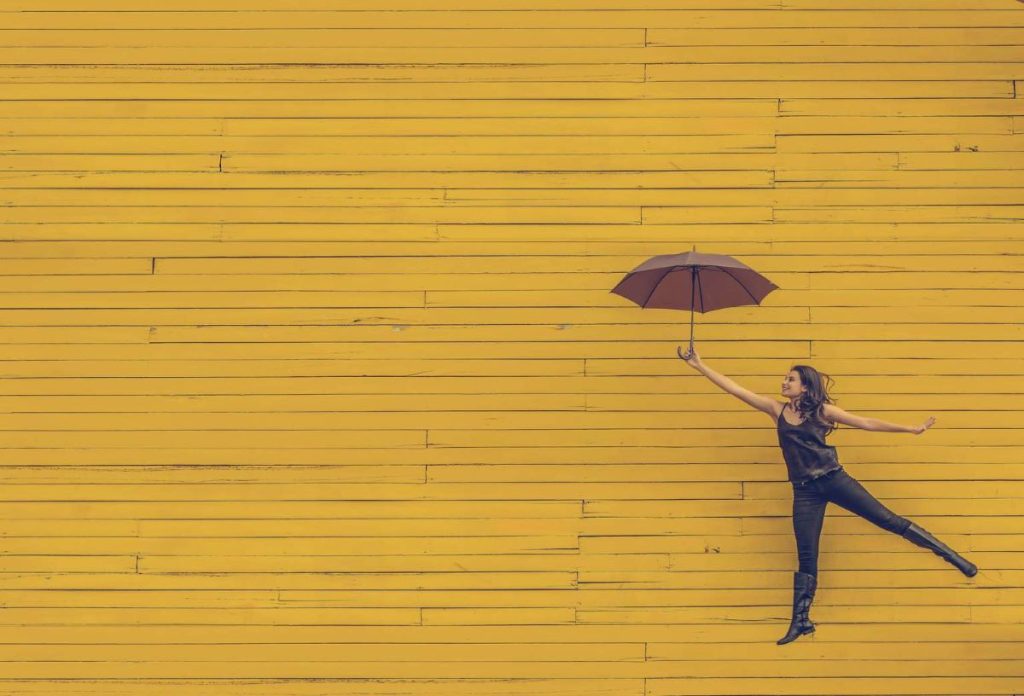 photo of a woman flying with an umbrella and a yellow background
