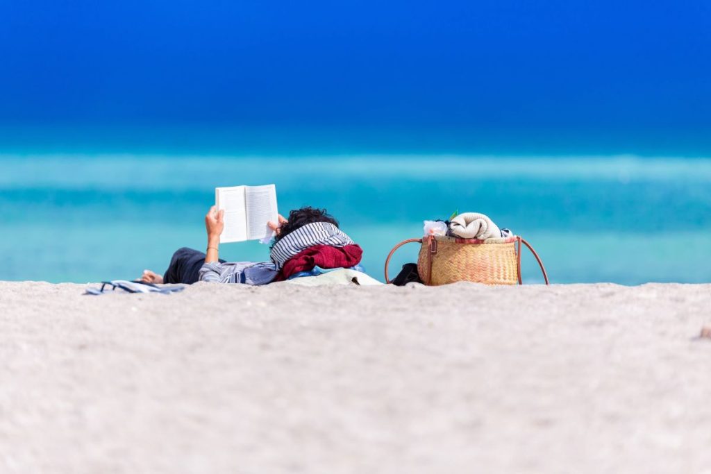 photo of a woman relaxing in the beach reading a book