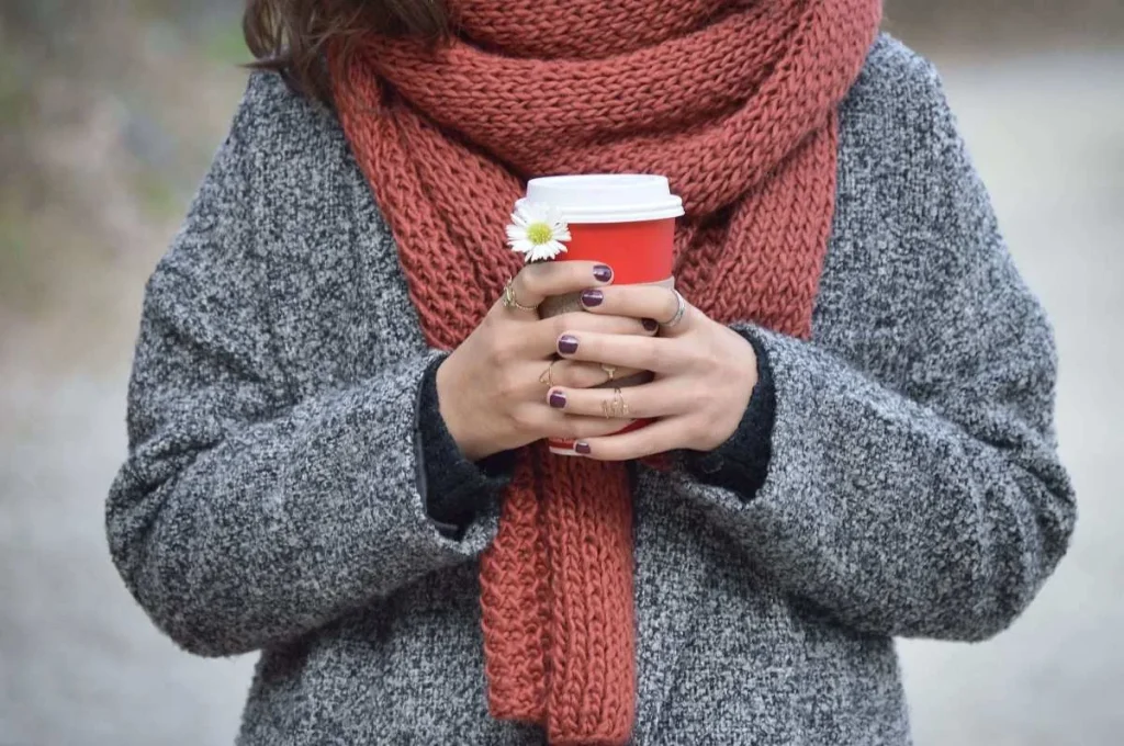photo of a woman wearing winter clothes while holding a hot cup of joe