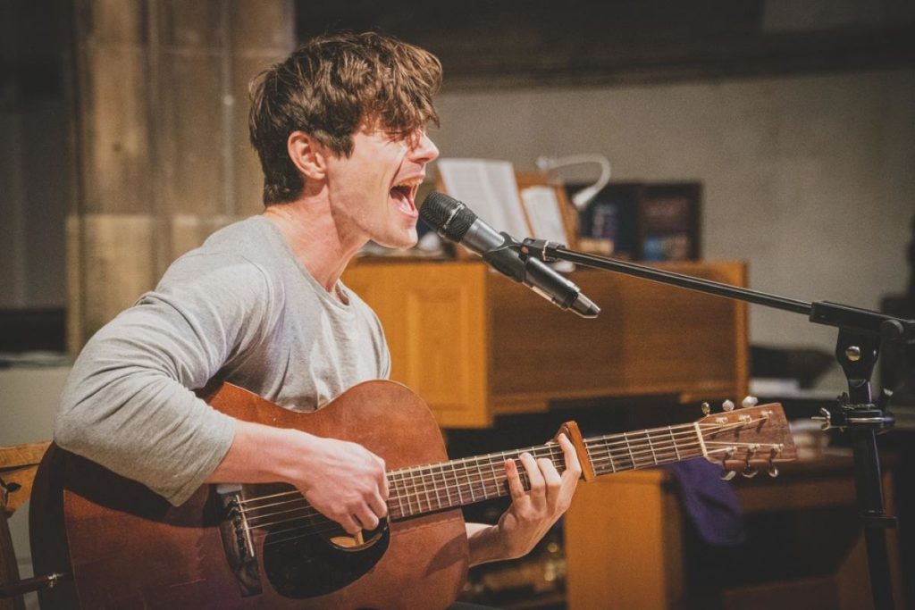 photo of a young man performing on stage singing and playing the guitar