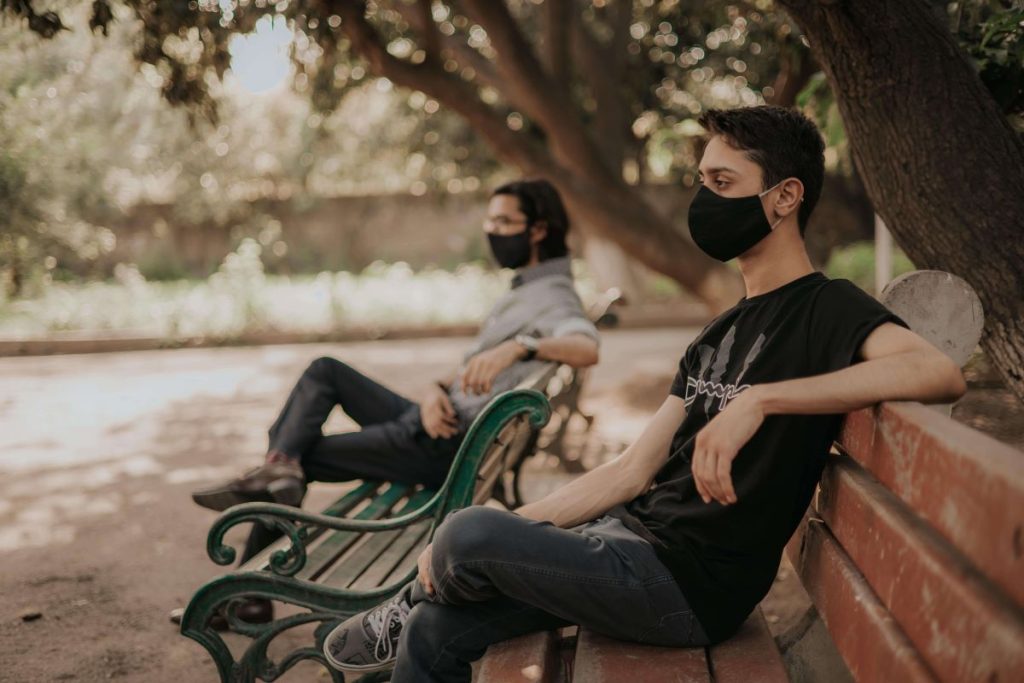 photo of two people sitting in a park bench wearing facemasks