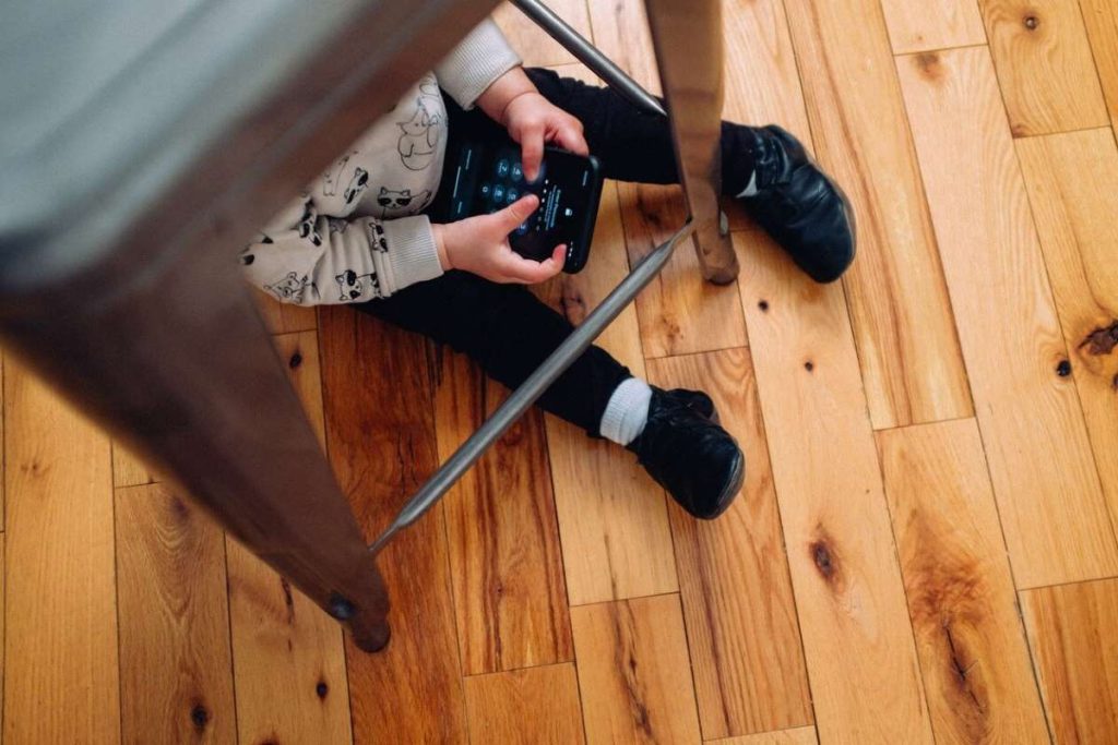 photo of a child playing with their gadget under a chair