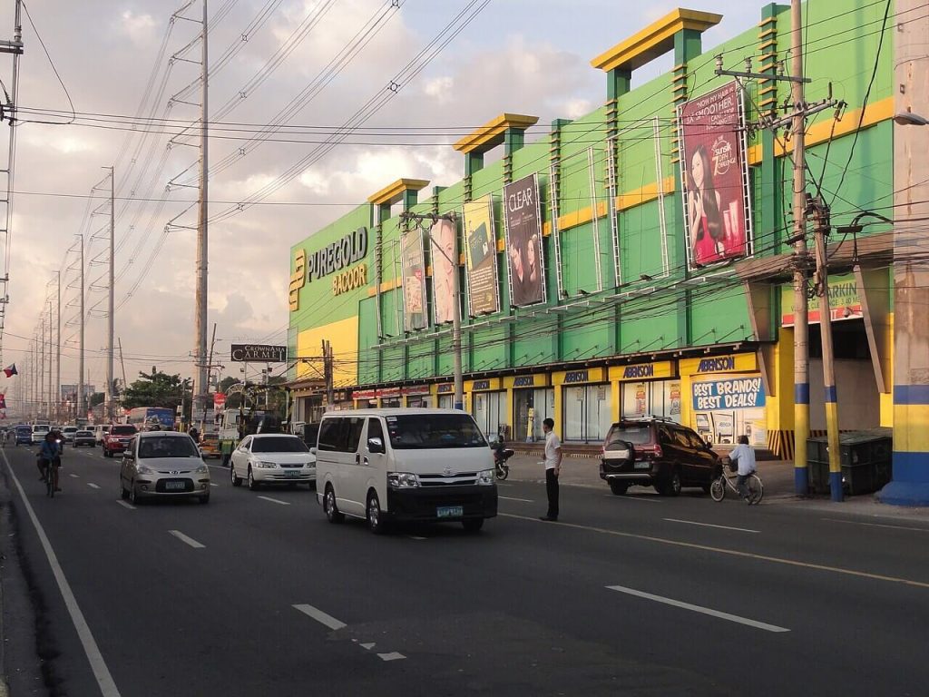 A busy commercial area in Bacoor, Cavite featuring the Puregold Bacoor building along Aguinaldo Highway, with multiple vehicles and people traveling key routes through the urban landscape; this photo highlights the accessibility and vibrant activity in the area, ideal to investors looking for real estate opportunities for sale in Bacoor, Cavite.